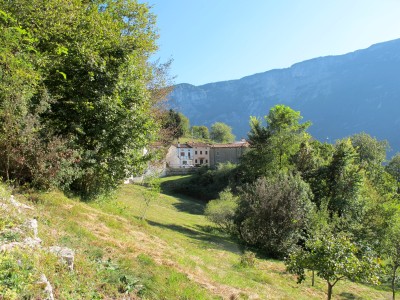 Dal fitto del verde, improvvisamente fa capolino Borgo Caloniche di Sotto, al di la di un prato soleggiato.